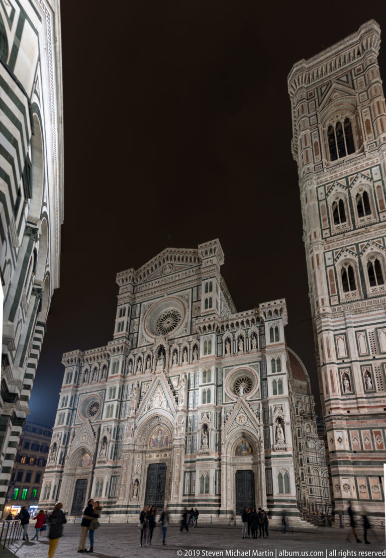 People crossing Piazza del Duomo before illuminated Florence Cathedral, with Giotto’s Campanile rising at right.