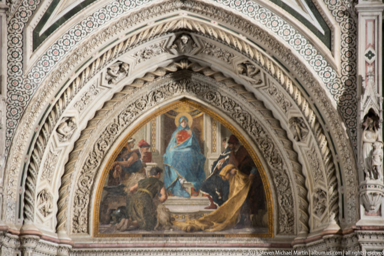 Pointed cathedral portal with enthroned Virgin and Child mosaic surrounded by layered carved arches and patterned marble.