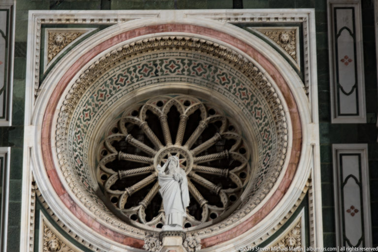 Circular rose window with radial stone tracery and concentric patterned marble bands on Florence Cathedral.