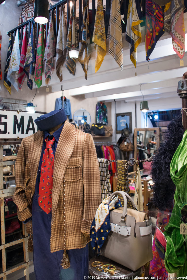 Headless mannequin wearing a brown checked jacket and red patterned tie beneath rows of colorful neckties.