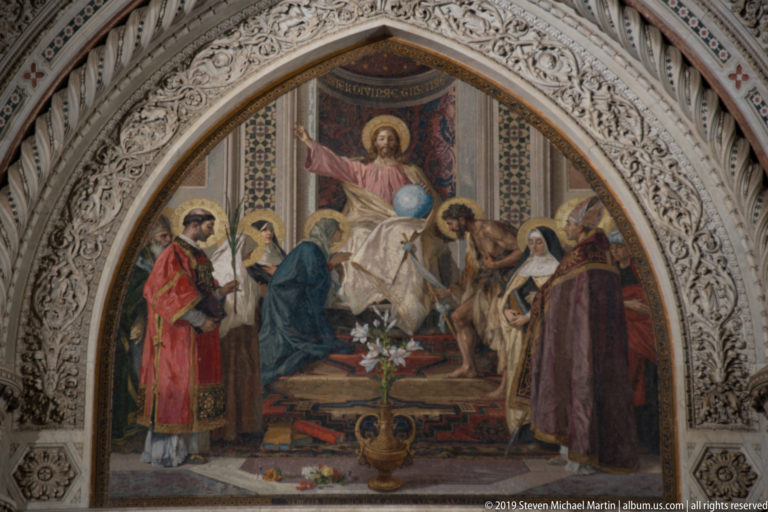 Colorful religious mosaic with a haloed central figure beneath carved pointed arches on Florence Cathedral.