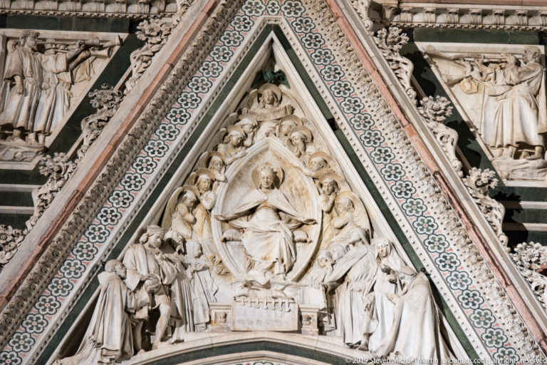 Triangular marble gable with Virgin and Child relief surrounded by figures and patterned stonework on Florence Cathedral.