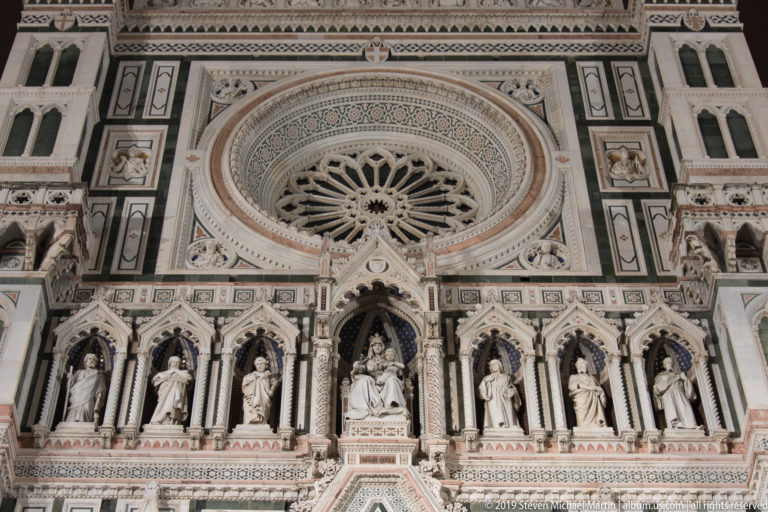 Large rose window and rows of sculpted niches on the illuminated upper façade of Florence Cathedral.