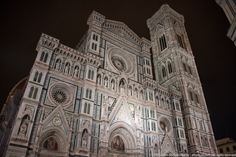 Low-angle nighttime view of Florence Cathedral’s ornate west façade with Giotto’s Campanile rising at right.