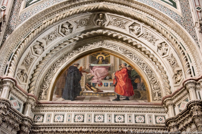 Three-figure mosaic lunette surrounded by deep concentric carved arches and patterned marble on Florence Cathedral.