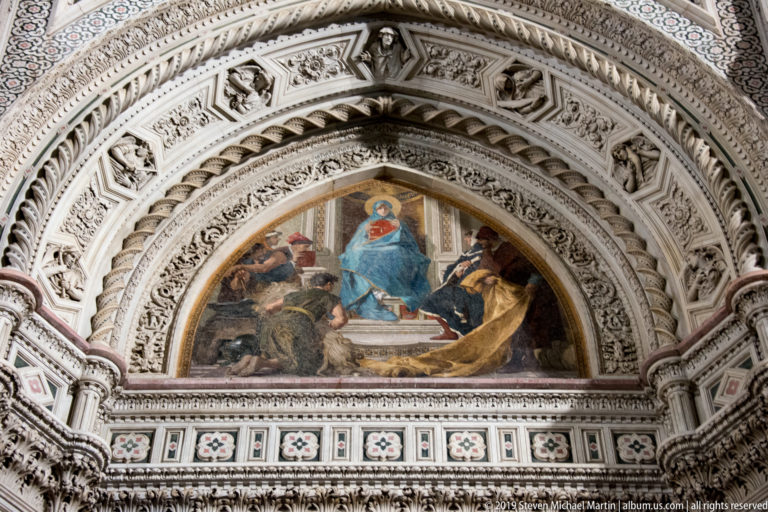Semicircular religious mosaic with a central blue-robed figure, surrounded by attendants and multiple bands of carved marble ornament.