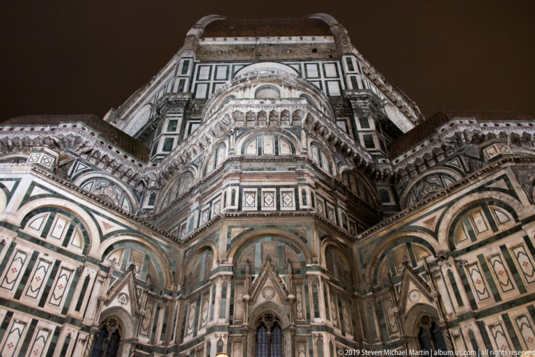 Steep low-angle nighttime view up Florence Cathedral’s polychrome marble exterior toward the great dome.