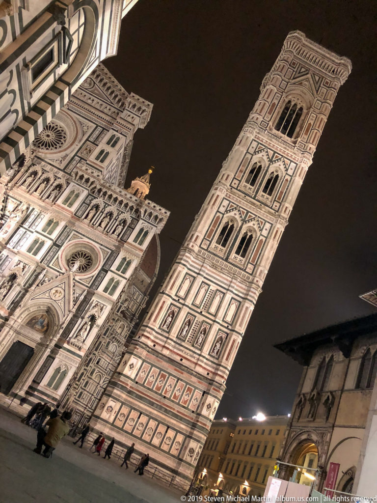 Low-angle nighttime view of Florence Cathedral’s marble façade beside the tall, illuminated Giotto’s Campanile.