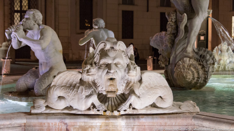 Close view of a bearded marine mask with open mouth and curling stone forms on the Fountain of Neptune.