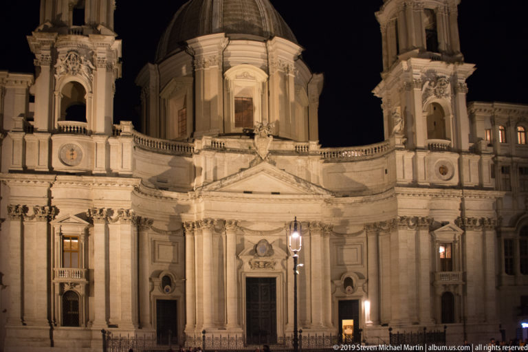 Illuminated Baroque façade, dome, and bell towers of Sant’Agnese in Agone against the night sky.