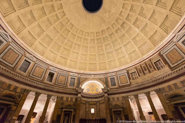 Sweeping Pantheon interior showing coffered dome, partial oculus, marble wall panels, columns, niches, and sanctuary around the rotunda.