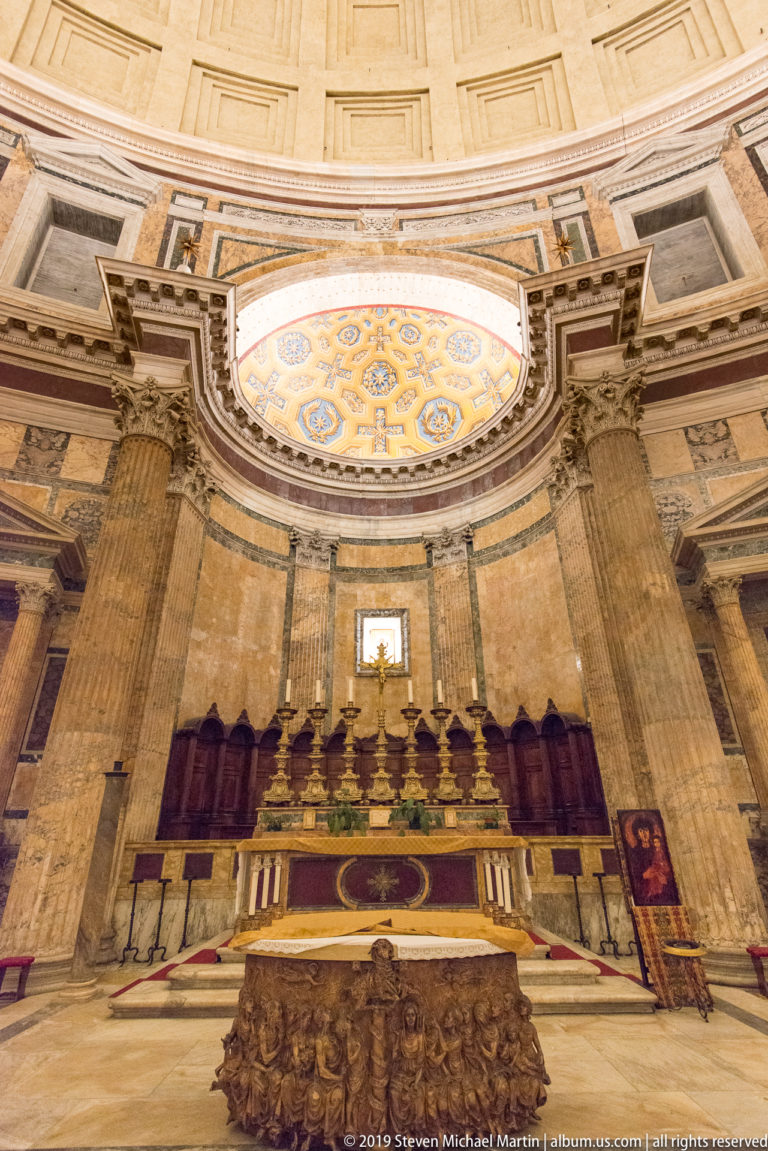 Wide Pantheon sanctuary with altar, gilded candlesticks, choir stalls, decorated apse, columns, and devotional image at right.