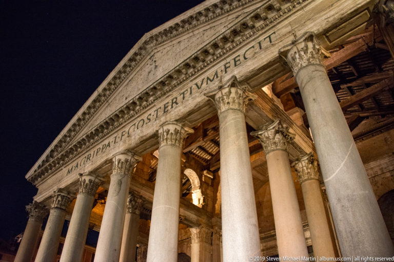 Angled night view of the Pantheon portico with Corinthian columns, triangular pediment, and the M·AGRIPPA inscription across the entablature.