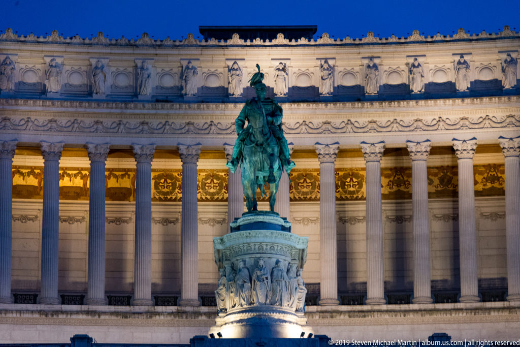 Bronze equestrian statue of Victor Emmanuel II centered before tall illuminated columns of the Vittoriano.