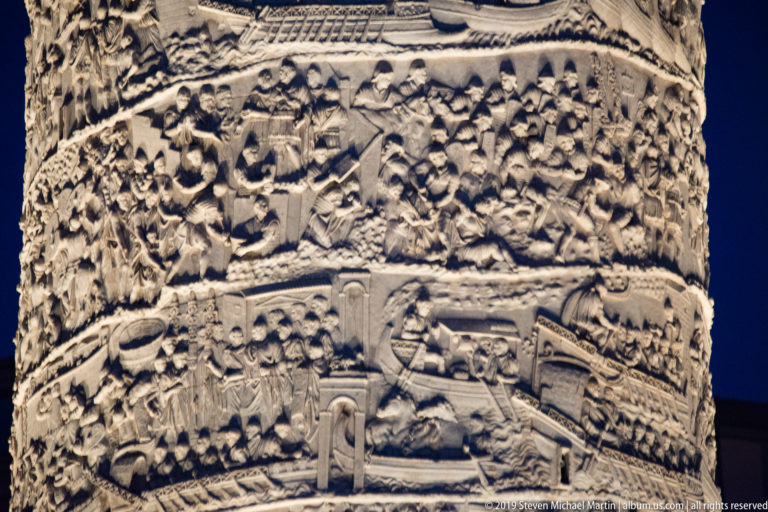 Several illuminated spiral bands on Trajan’s Column filled with carved soldiers, buildings, equipment, and changing terrain.