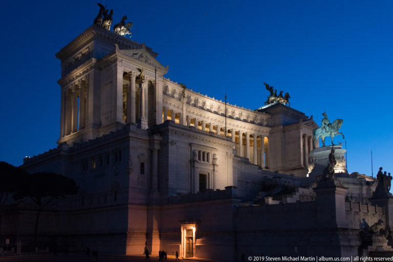 Illuminated Vittoriano at night with the equestrian statue of Victor Emmanuel II silhouetted before its long white marble façade.