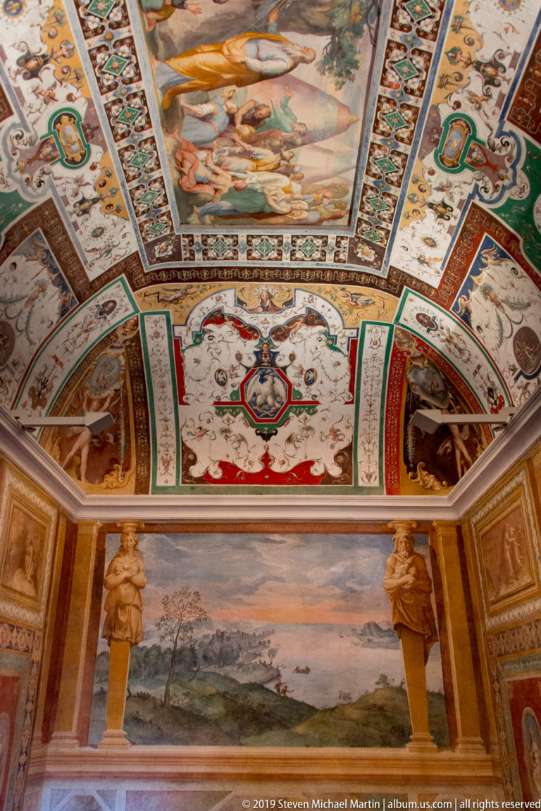 Oblique interior view of a frescoed vault above a large landscape panel, with painted figures and ornate borders.