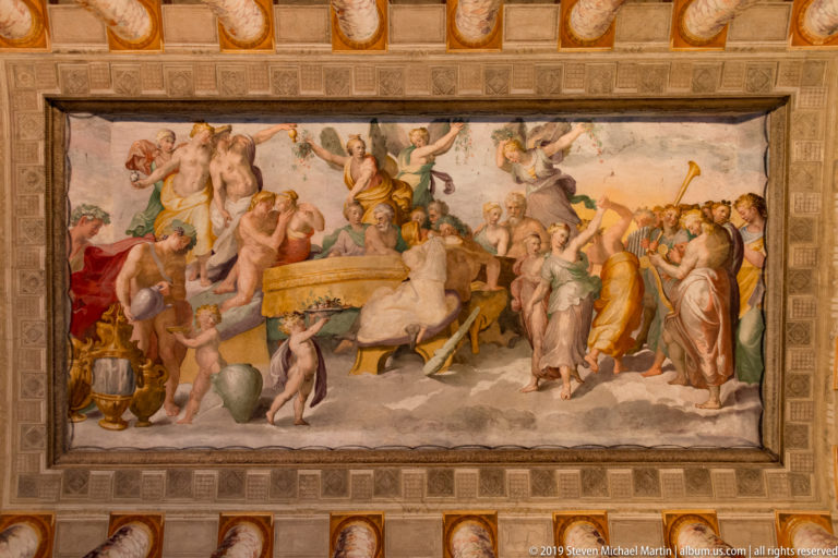 Crowded classical fresco with robed figures, musicians, vessels, and attendants gathered around a central altar.