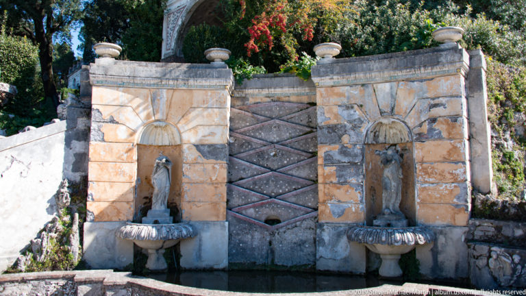 Paired arched niches with standing statues and shell basins separated by a patterned central panel.