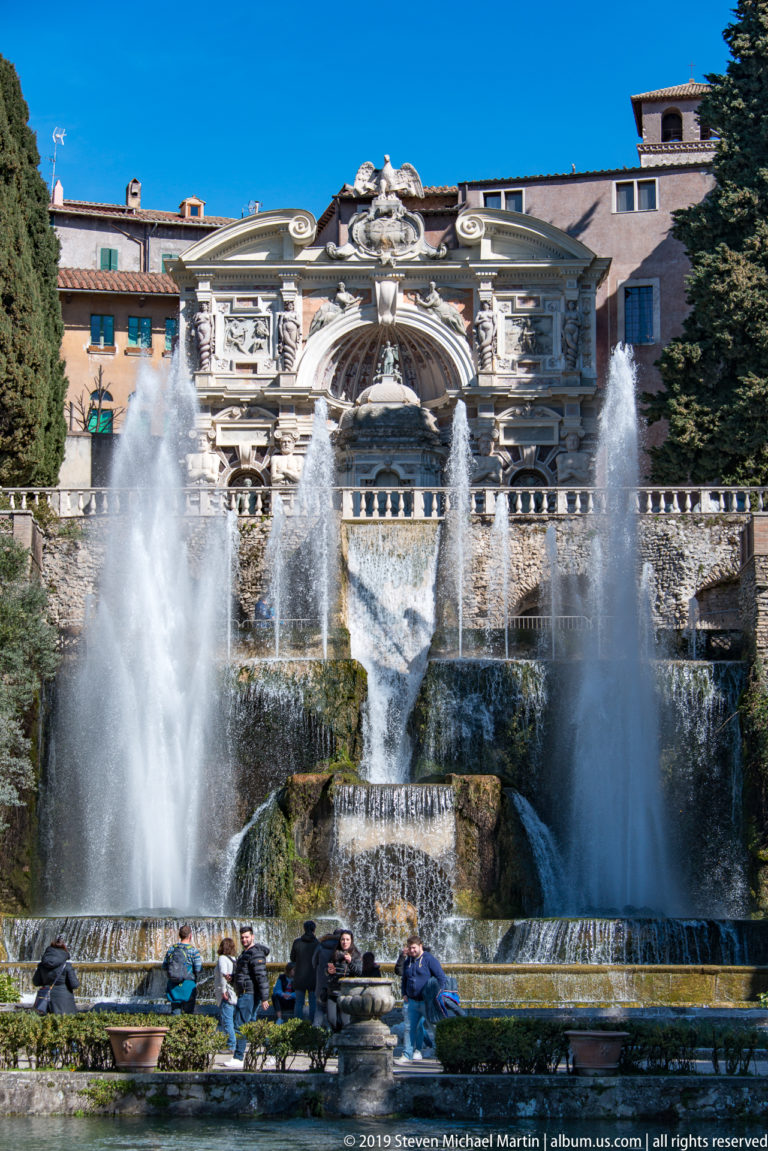 Visitors seated before a monumental tiered cascade with twin fountain jets and ornate architecture.
