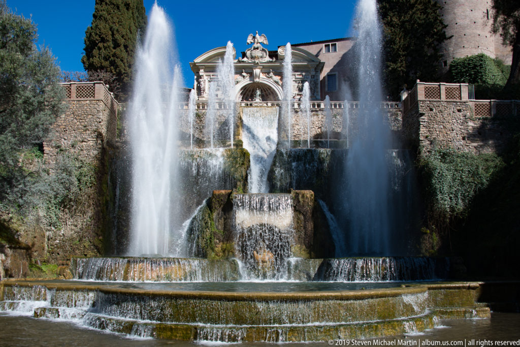 Large tiered cascade with twin high fountain jets and ornate architectural fountain façade above.