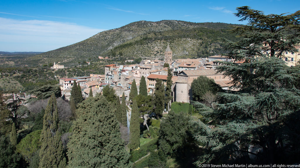 Panoramic view of Tivoli’s historic buildings, church towers, cypresses, and wooded slopes beneath a rugged mountain.