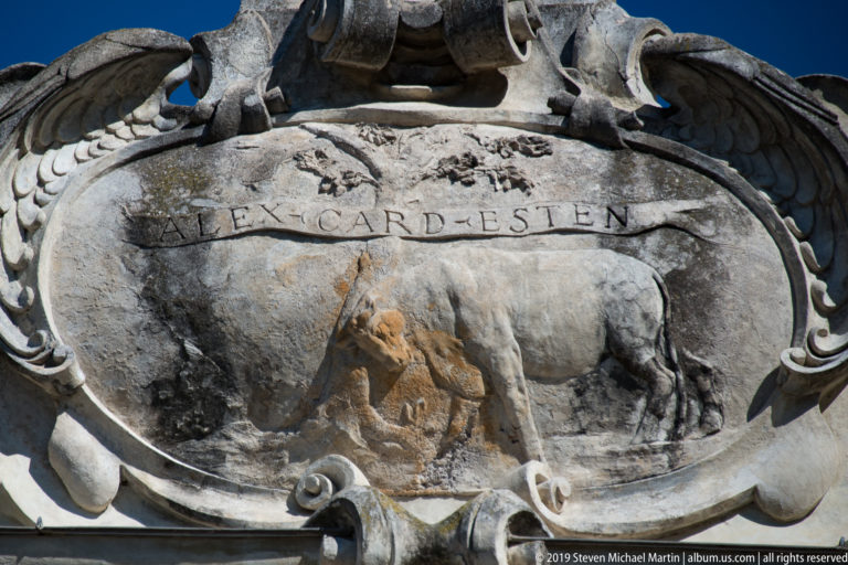 Close view of a weathered stone cartouche with incised lettering, worn relief, and deep scrolling borders.