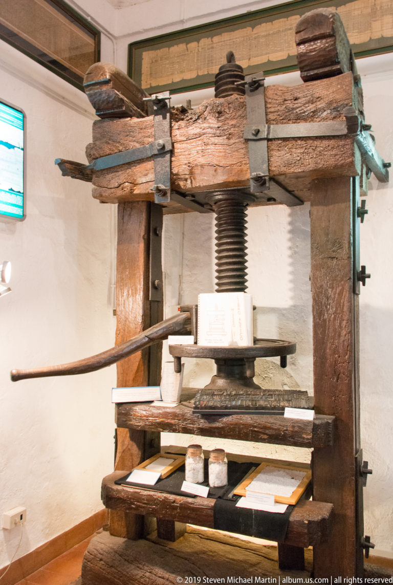 Large wooden hand printing press with screw spindle, platen, bed, iron fittings, and long operating bar.