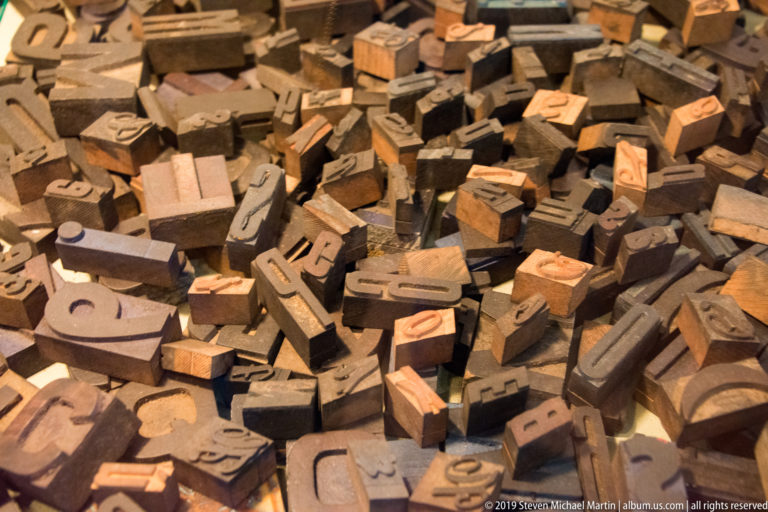 Pile of rectangular printing type blocks with raised letters, numerals, and punctuation visible on their ends.