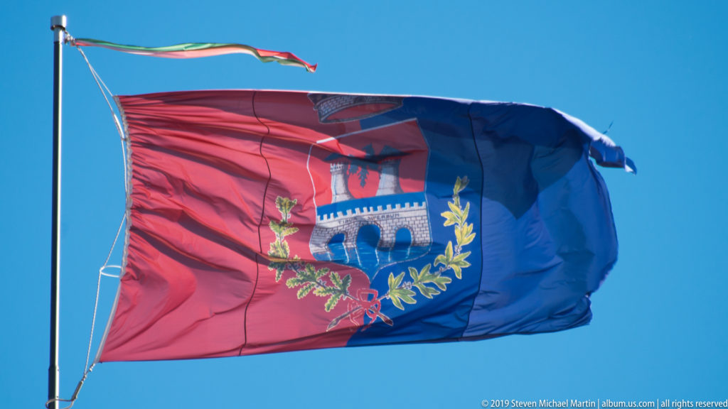 Red-and-blue Tivoli civic flag with heraldic emblem flying beneath a small Italian tricolor streamer.