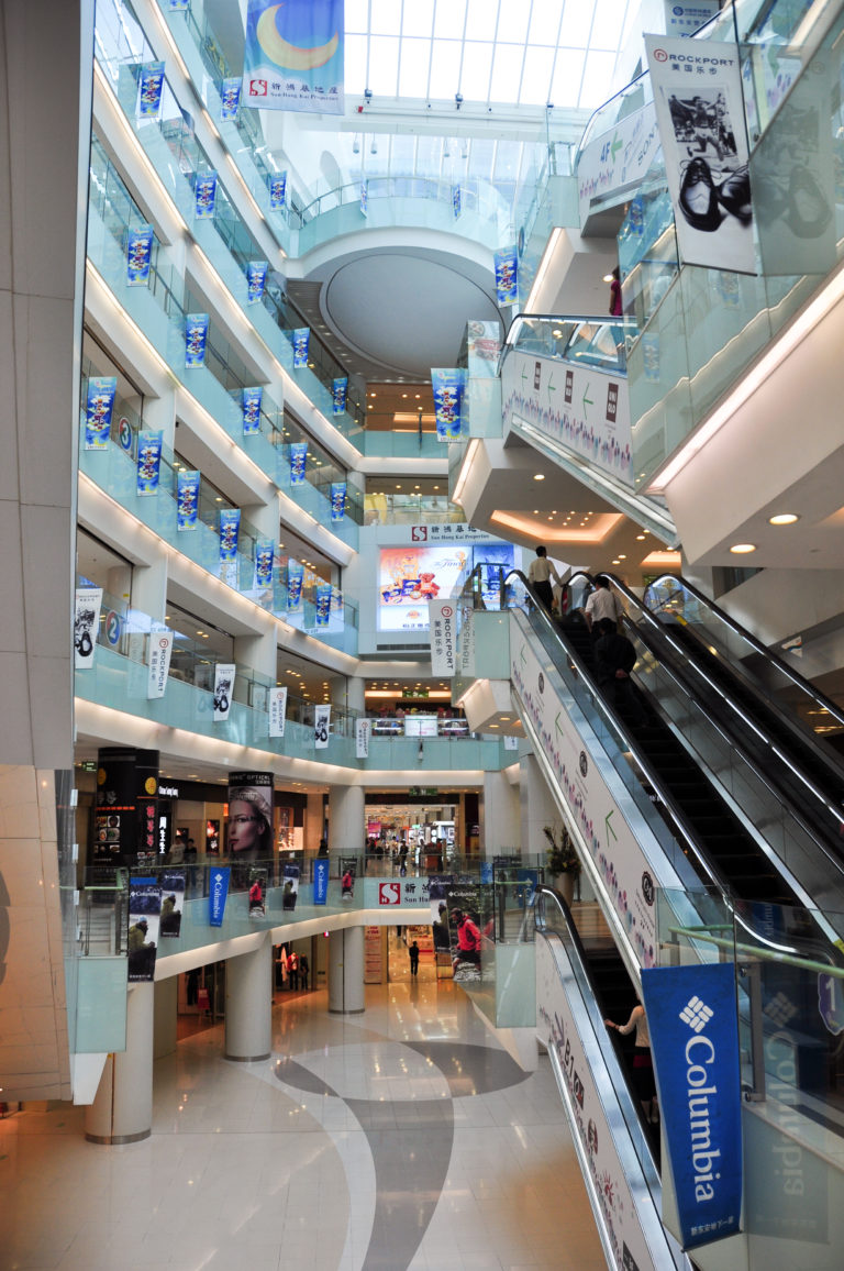 Escalators and open balconies inside the bright multi-level atrium of a modern Beijing department store.