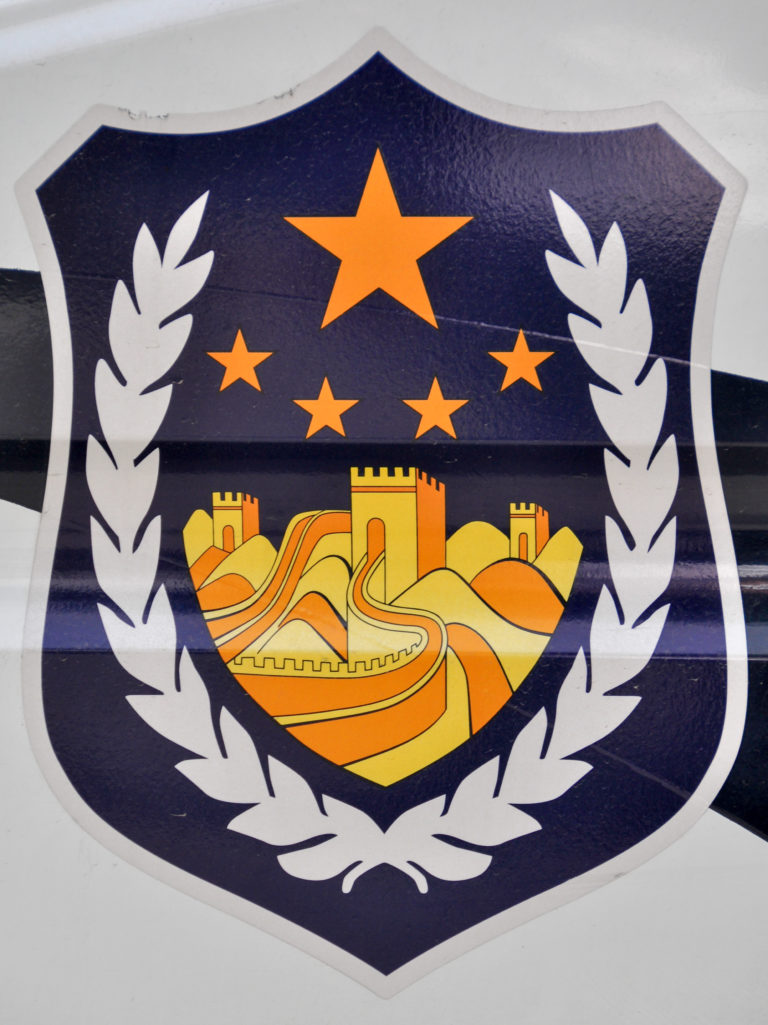 Graphic emblem of a stylized orange Great Wall inside a dark blue shield, flanked by white laurel branches and topped with five orange stars.