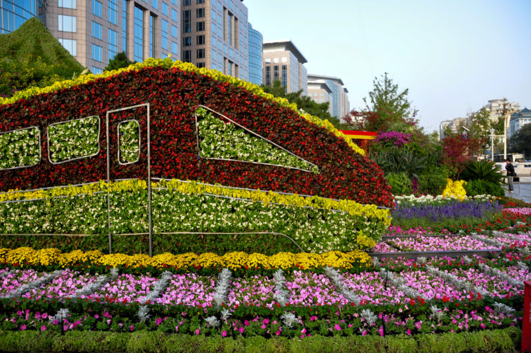 Large geometric floral installation surrounded by multicolored flower beds, with modern Beijing buildings rising in the background.