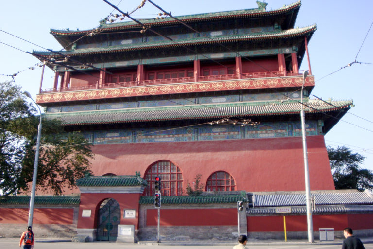 Exterior of the Beijing Bell Tower with a red masonry base and green-tiled timber pavilion at a street intersection.