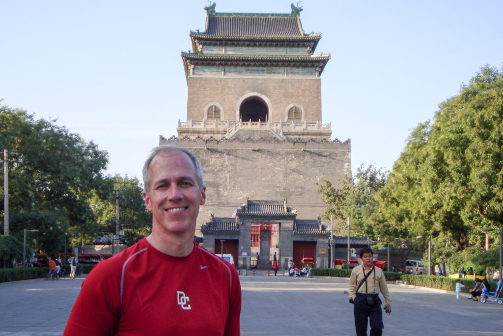 Smiling man in a red shirt standing in front of Beijing’s Drum Tower in Beijing.