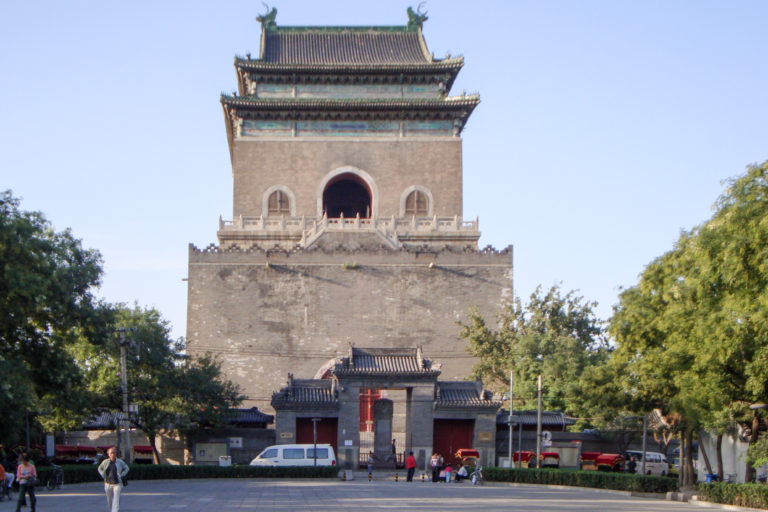Beijing Drum Tower seen from the forecourt, with a monumental gray-brick base supporting a tall timber pavilion with a dark tiled roof and a large central arched opening.