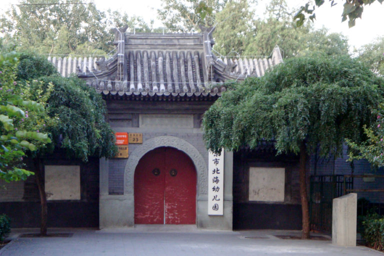 Traditional gray-brick courtyard gate with red double doors partly covered by vines.