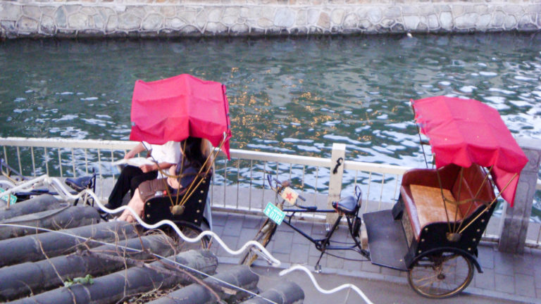 Two red-canopied pedicabs parked by a canal in Beijing’s Houhai area.