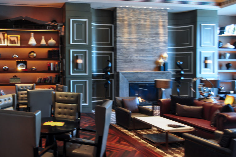 Contemporary Beijing hotel lounge with dark leather seating around low tables in front of a tall stone fireplace and built-in shelves with decorative objects.