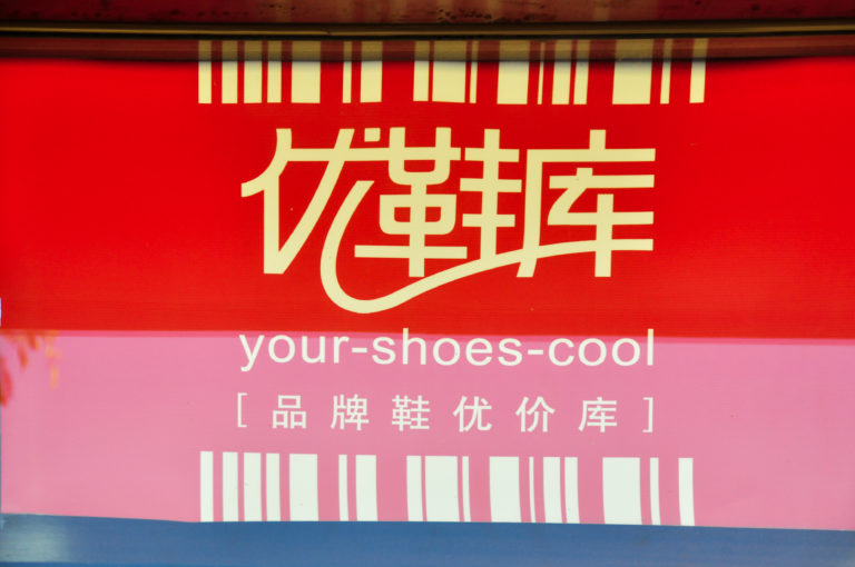 Bright red commercial sign reading “your-shoes-cool” with stylized Chinese characters on a Beijing shoe store.