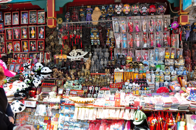 Densely packed Beijing souvenir stall with panda toys, Chinese opera masks, figurines, jewelry, and framed images filling the storefront.