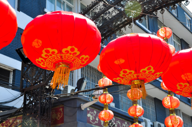 Large red lanterns with gold patterns and tassels hanging over a Beijing market street.