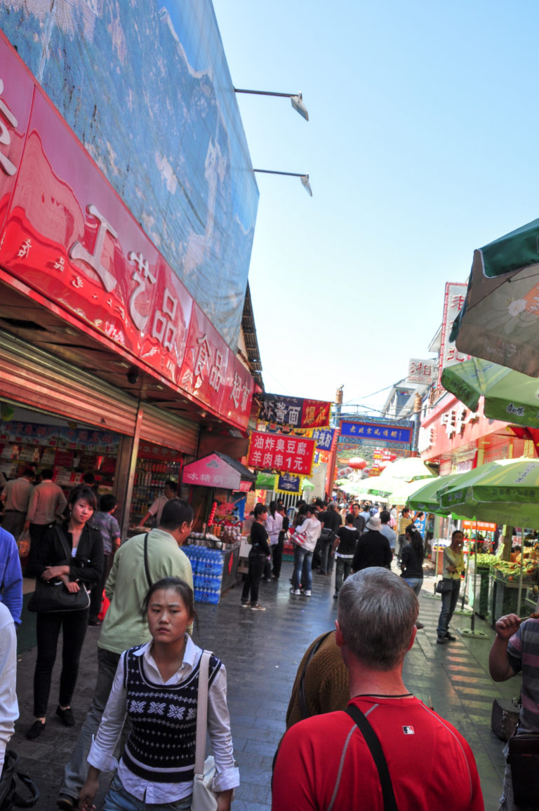 Crowded Beijing food street filled with pedestrians, food stalls, and dense restaurant signs.