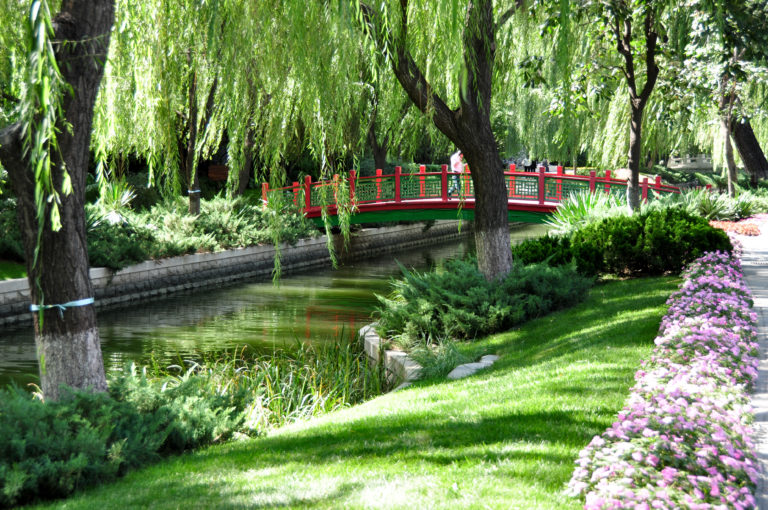 Small red footbridge over a willow-lined canal in a Beijing park.