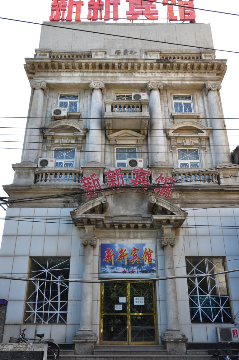 Ornate multi-story facade of the 新新宾馆 in Beijing, with red Chinese characters and Western-style arches, balconies, and columns.