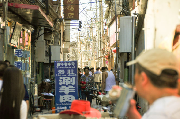 Crowded Beijing hutong alley with small shops and a sign advertising instant boiled tripe.