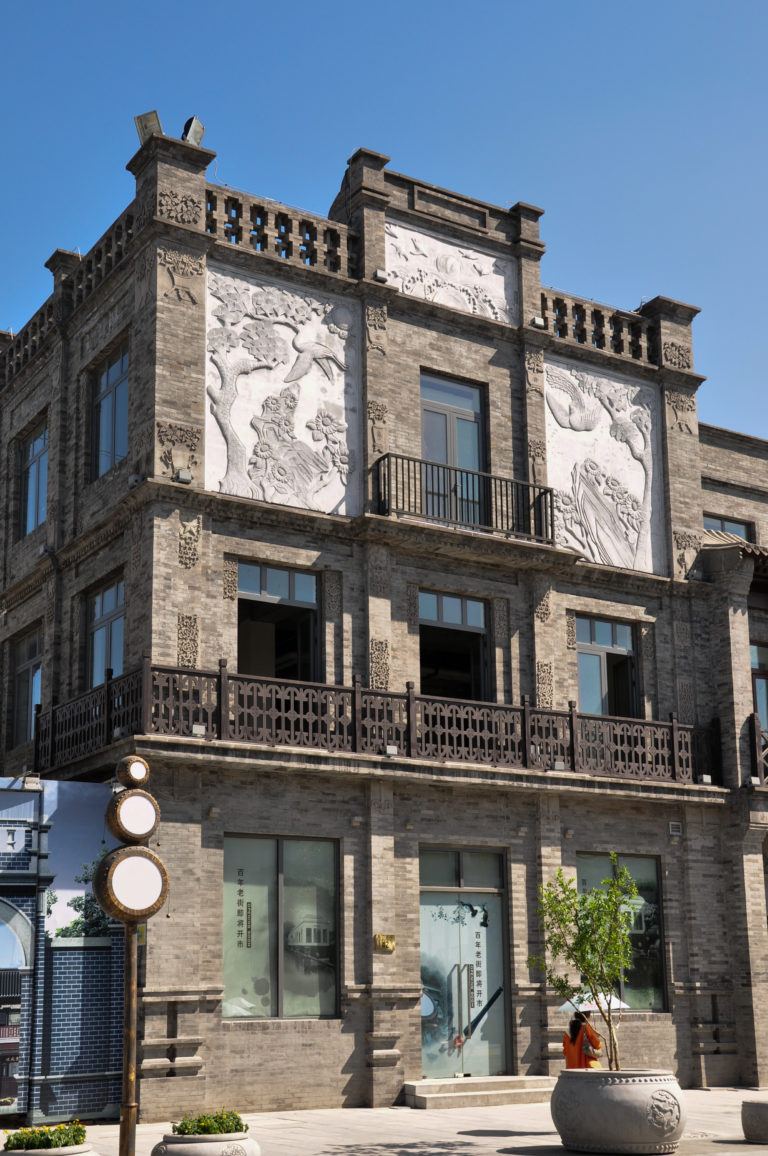 Gray-brick commercial building with large pale relief panels and dark metal balconies in a Beijing historic district.