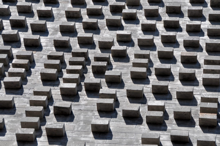Gray brick wall in Beijing with staggered projecting bricks casting geometric shadows.