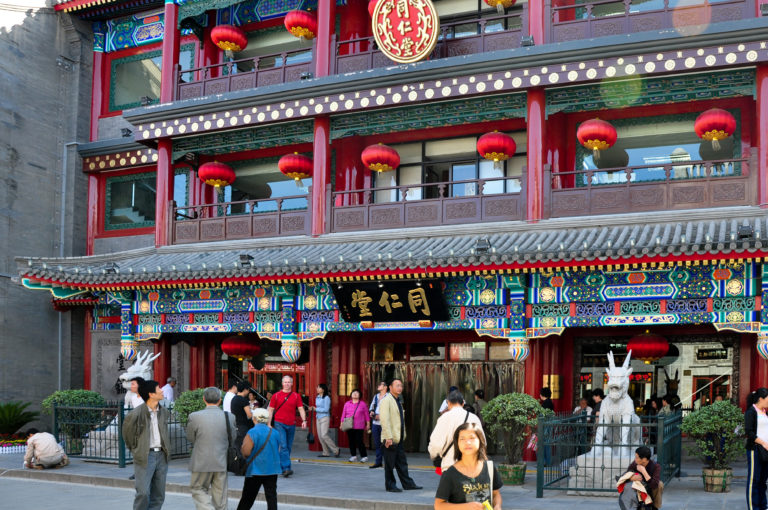 Ornate facade of a historic Beijing Tongrentang Chinese medicine store, with a black-and-gold 同仁堂 sign and red lanterns.