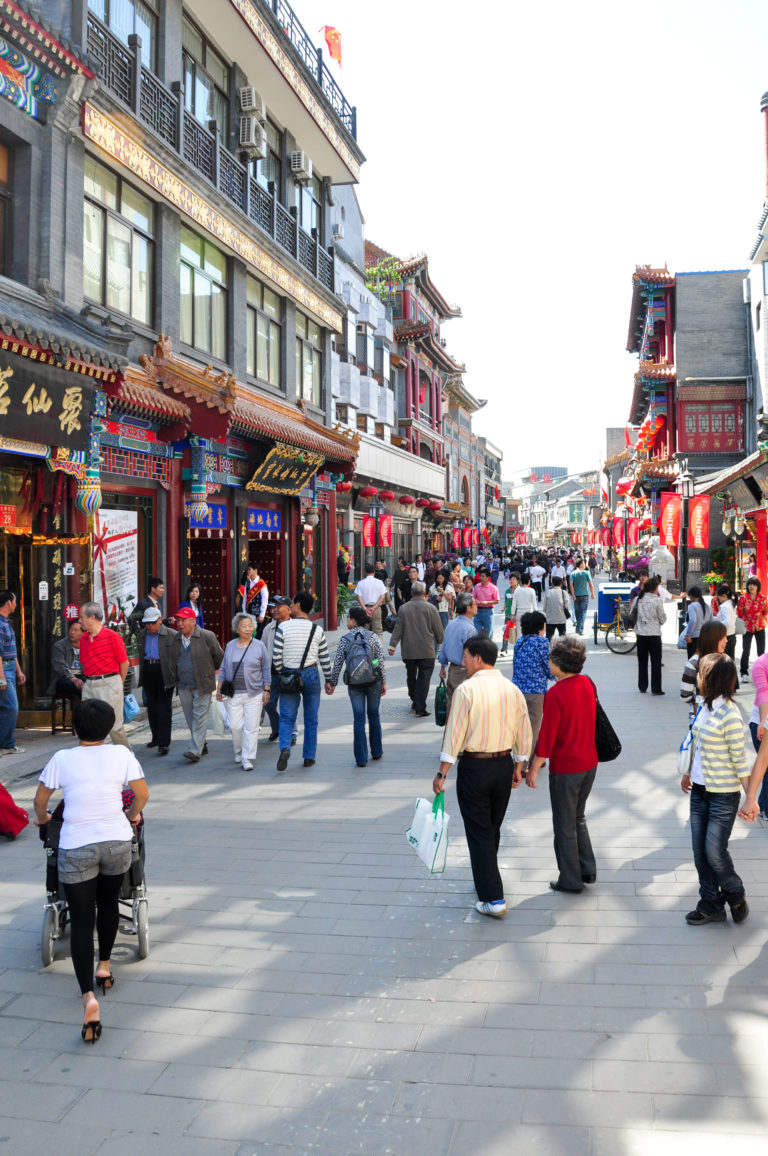 Crowded traditional-style pedestrian shopping street in central Beijing lined with colorful shops and red lanterns.
